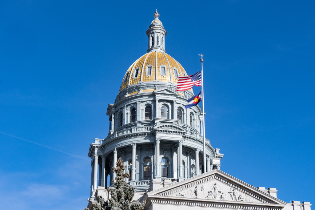 Gold exterior dome of the Colorado State Capitol building in Denver with flags flying